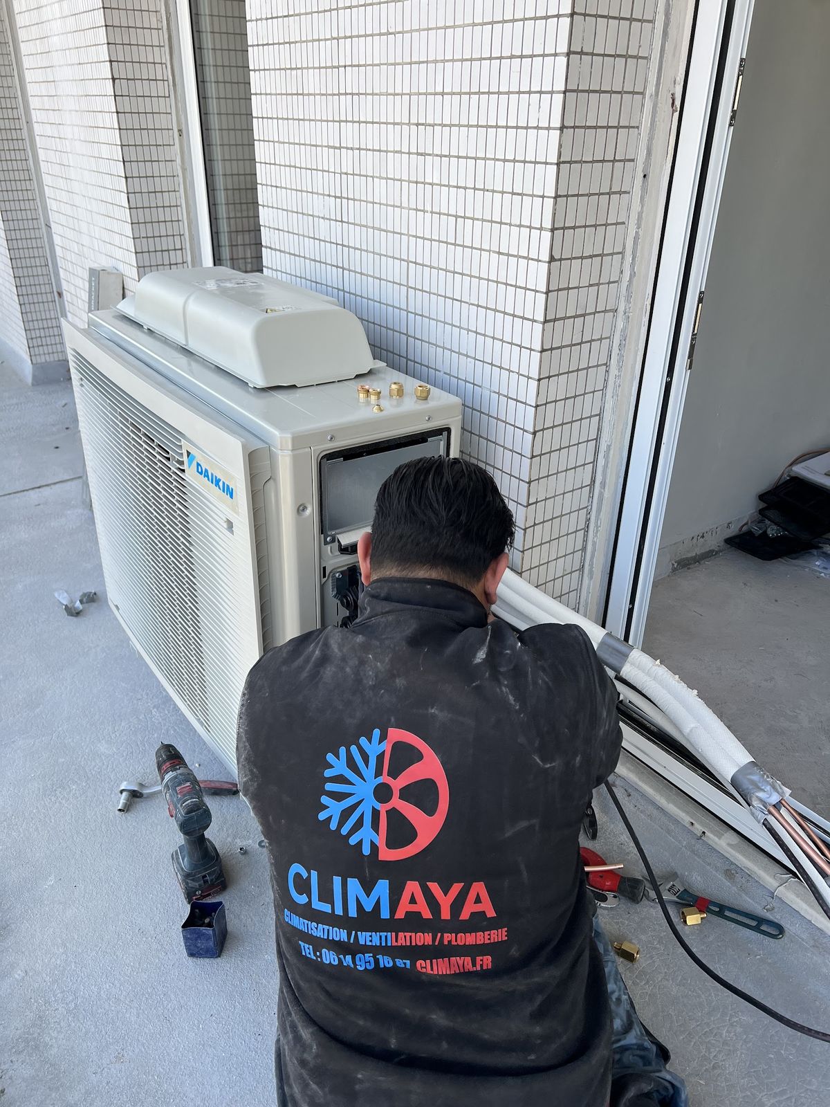Technicien Climaya, le logo au dos, au travail sur un groupe extérieur Daikin, sur un balcon