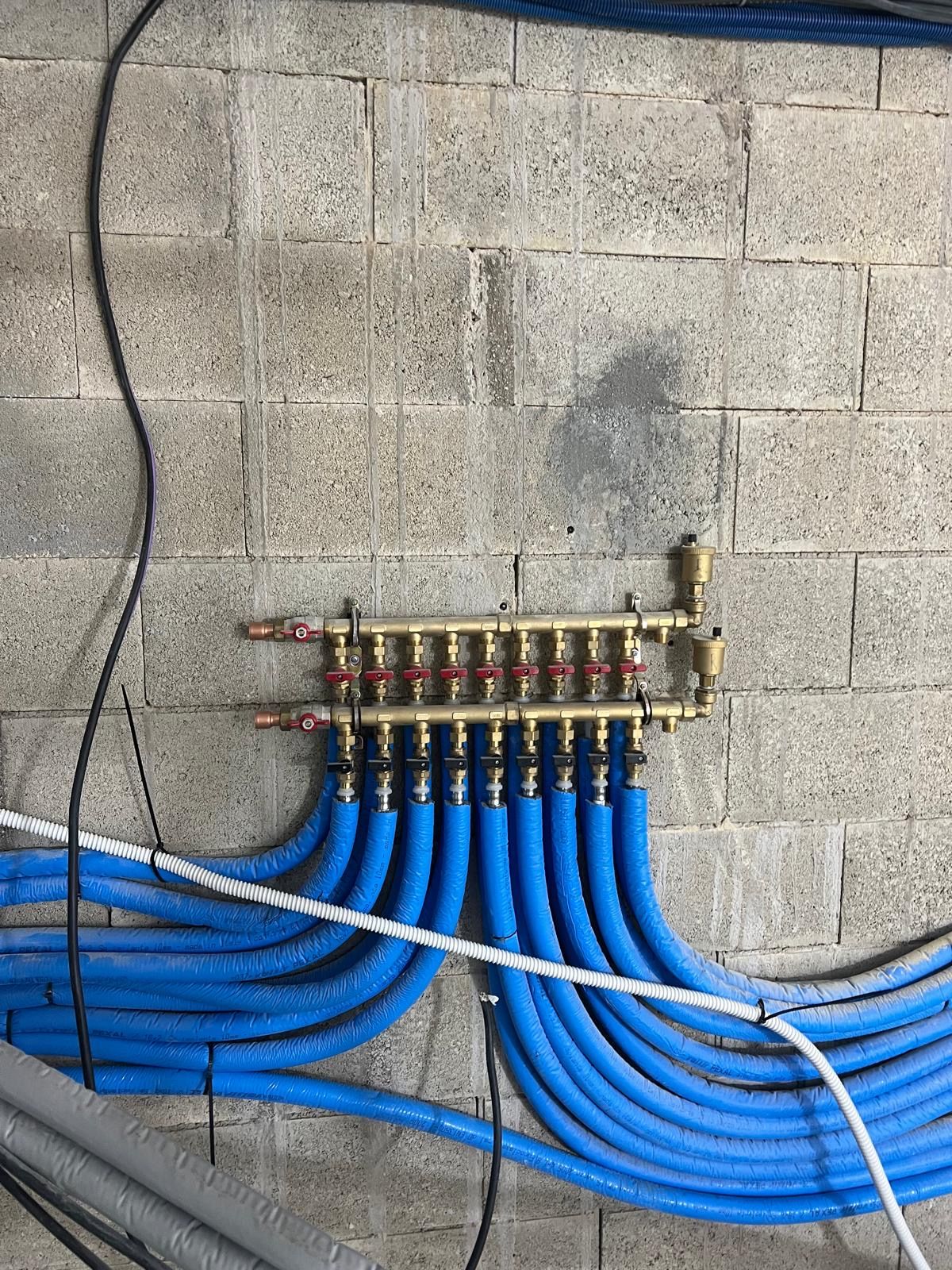 Collecteur en laiton et départs isolés en bleu, le long d'un mur en parpaings
