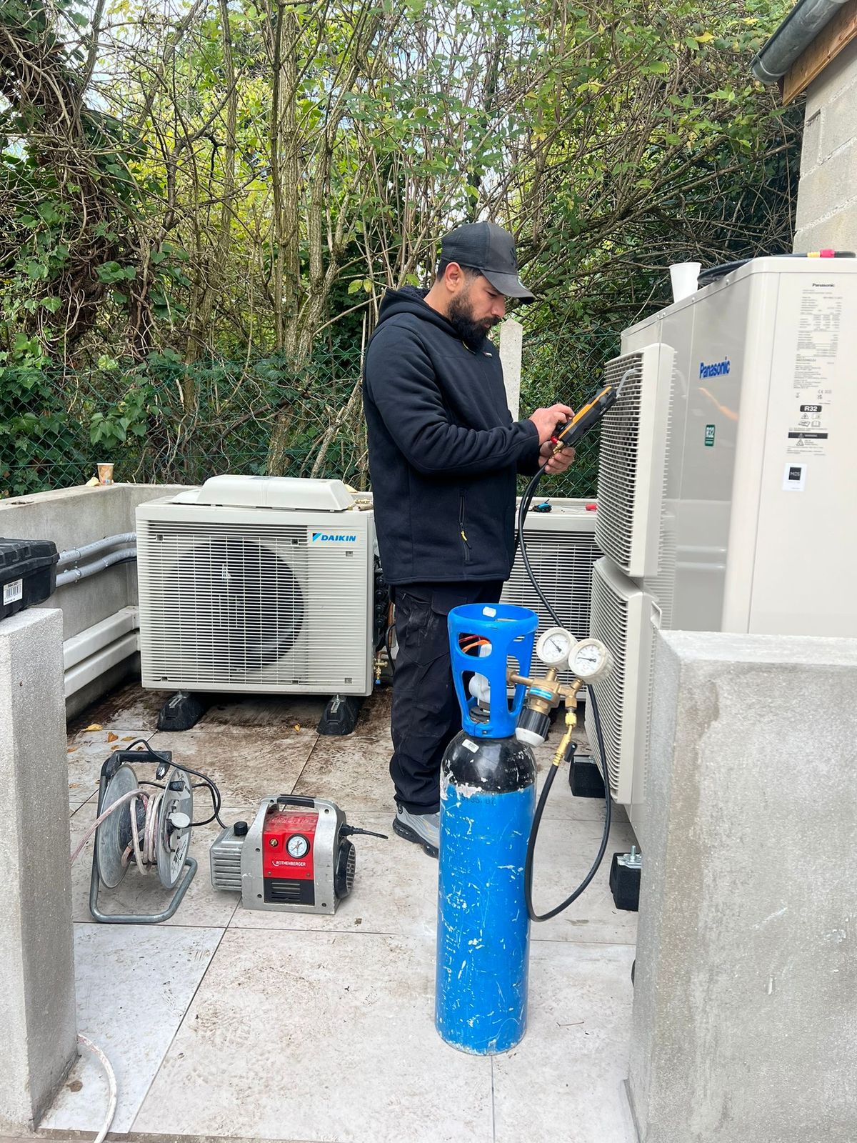 Technicien relié aux manomètres, avec bouteille d'azote et pompe à vide, devant des groupes Daikin et Panasonic