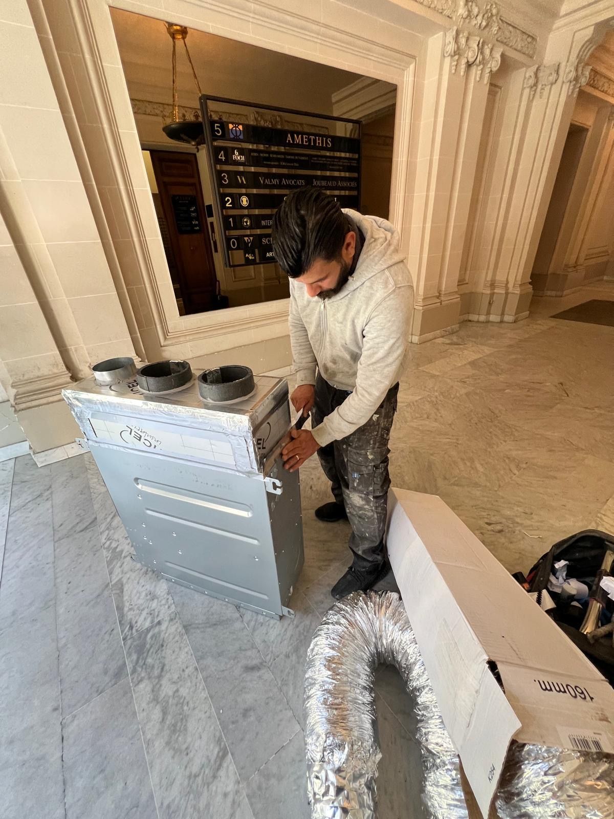 Technicien préparant une unité gainable et son plénum dans le hall en pierre d'un immeuble de bureaux