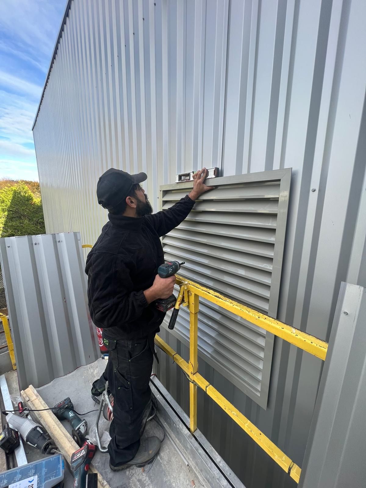 Technicien sur une nacelle, posant une grille de ventilation sur un bardage métallique