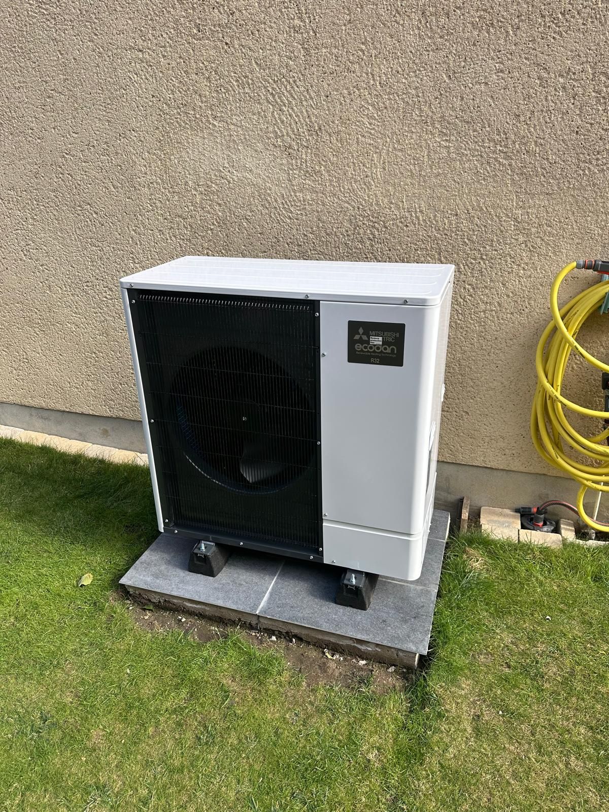 Pompe à chaleur air-eau Mitsubishi Electric Ecodan posée sur une dalle et des plots, au pied d'une maison